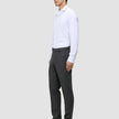En man klädd i en vit skjorta, byxor av modellen Motion Suit Pants Regular Pepper Grey och svarta loafers i en ren skandinavisk design.