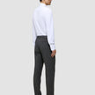 En man sedd bakifrån, klädd i en vit skjorta med knappar, Motion Suit-byxor i storlek Regular i färgen Pepper Grey samt svarta loafers.