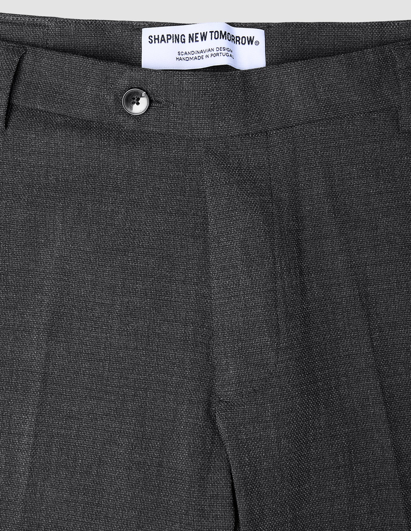 Närbild på de kolgrå Motion Suit-byxorna i modell Regular Pepper Grey med en knapp och en märkesetikett i midjan.