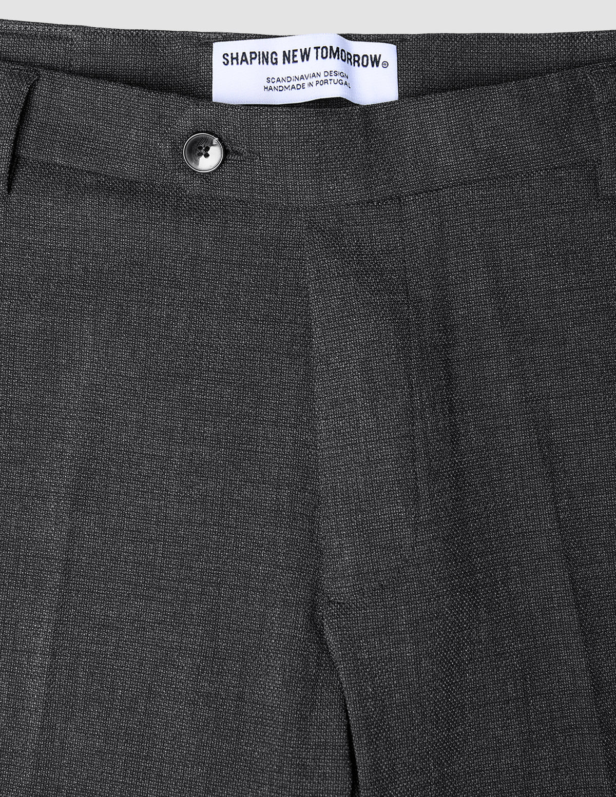 Närbild på de kolgrå Motion Suit-byxorna i modell Regular Pepper Grey med en knapp och en märkesetikett i midjan.