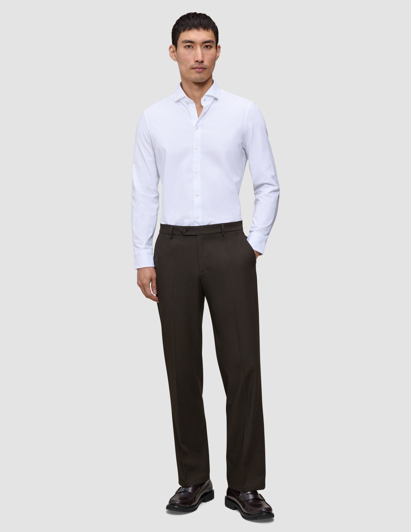 En man i en vit skjorta, Motion Suit-byxor i modell Relaxed i färgen Cognac och mörka loafers.