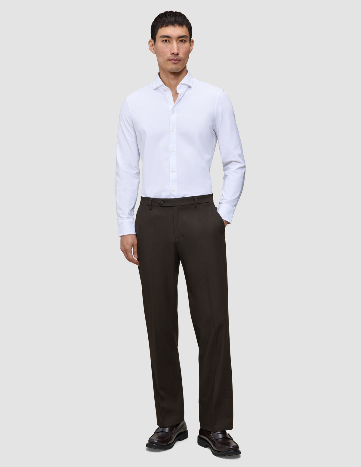 En man i en vit skjorta, Motion Suit-byxor i modell Relaxed i färgen Cognac och mörka loafers.