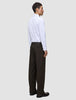 En person klädd i en vit skjorta med knappar och bruna Motion Suit-byxor i modellen Relaxed Cognac med 360°-stretch.