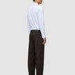 En person klädd i en vit skjorta med knappar och bruna Motion Suit-byxor i modellen Relaxed Cognac med 360°-stretch.