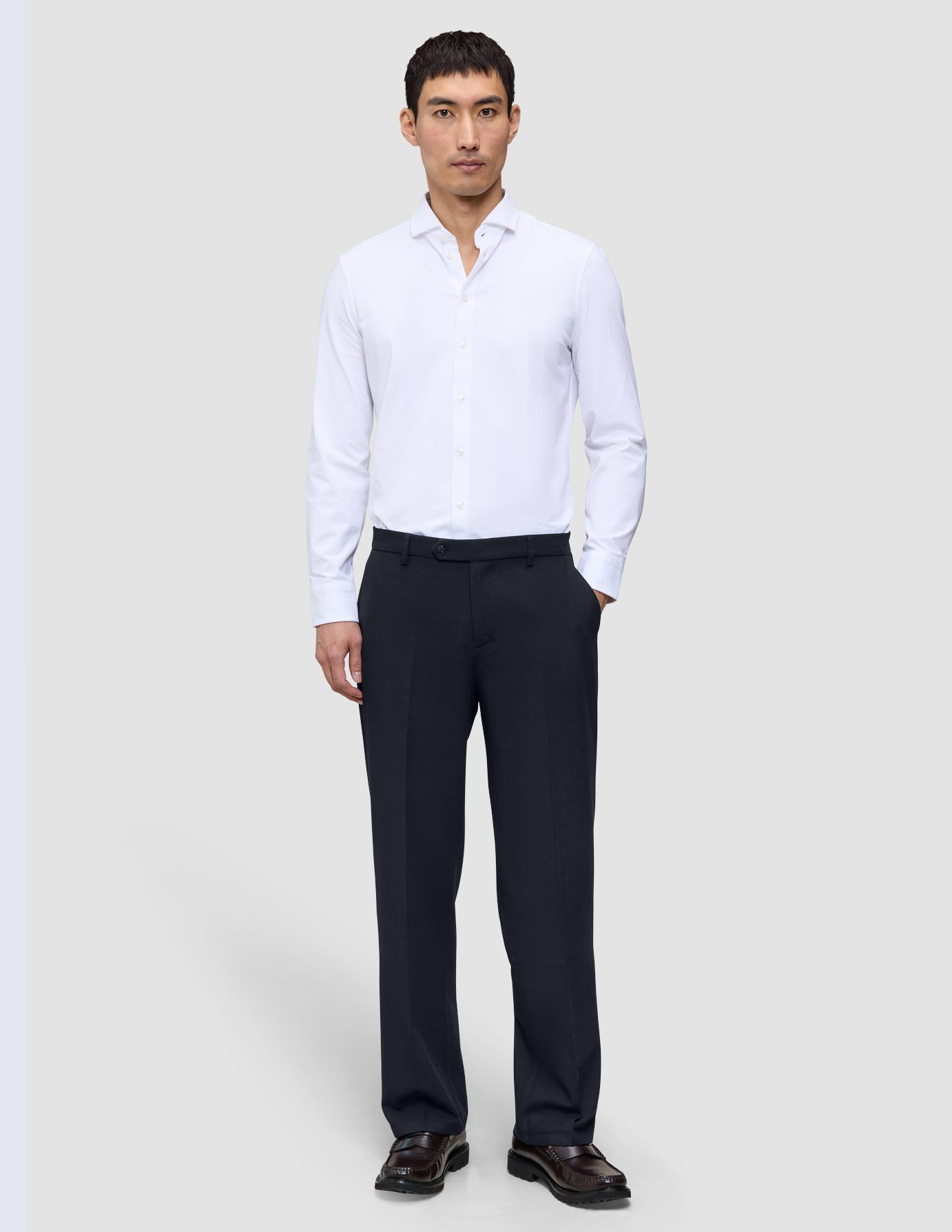 En man bär en vit skjorta med knappar och ett par Motion Suit-byxor i modell Relaxed i färgen Midnight Blue med 360°-stretch.