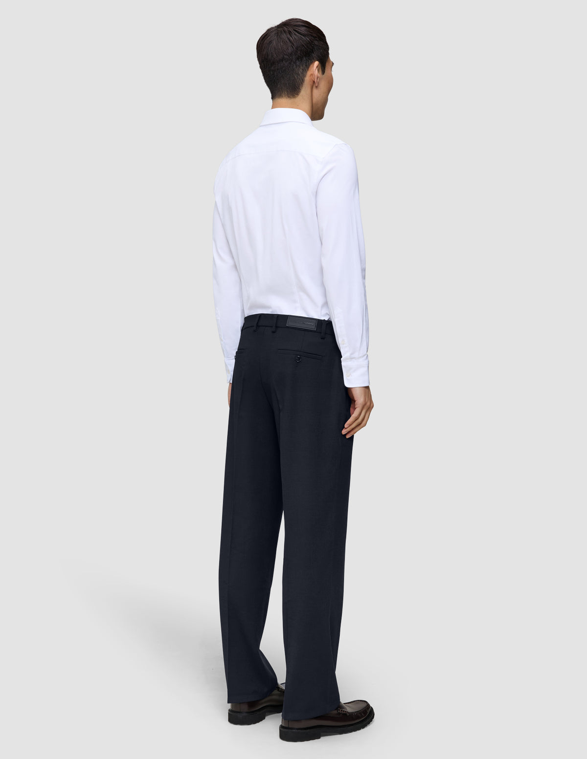 En person sedd bakifrån, klädd i en vit skjorta med knappar och ett par Motion Suit-byxor i modell Relaxed i färgen Midnight Blue.
