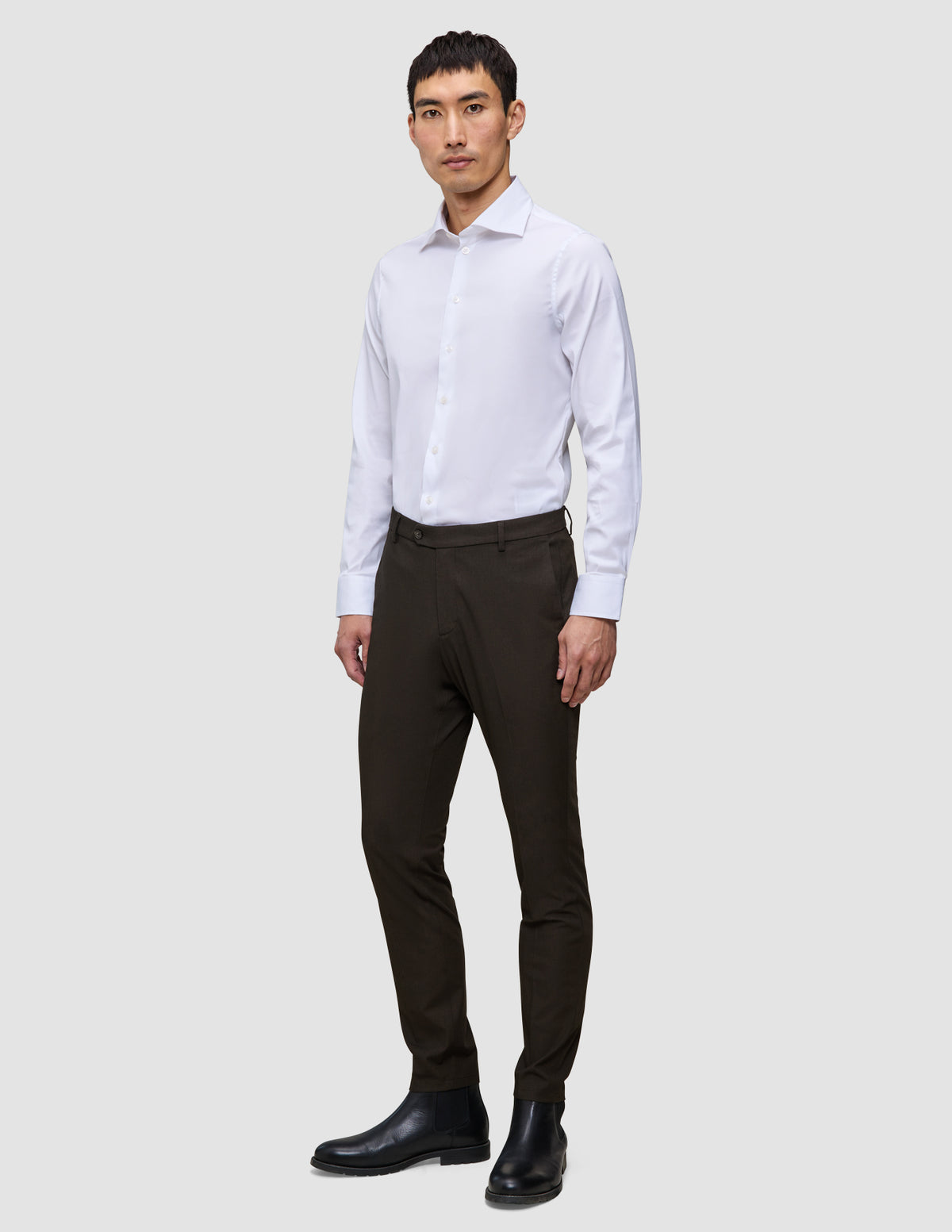 Man i en vit skjorta, Motion Suit-byxor i smal passform i färgen Cognac med 360°-stretch och svarta stövlar.