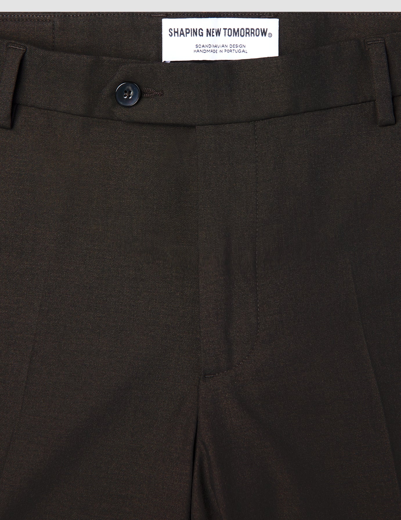Närbild på de bruna Motion Suit-byxorna i modell Slim Cognac med 360°-stretch, knäppning och en inbyggd märkesetikett.
