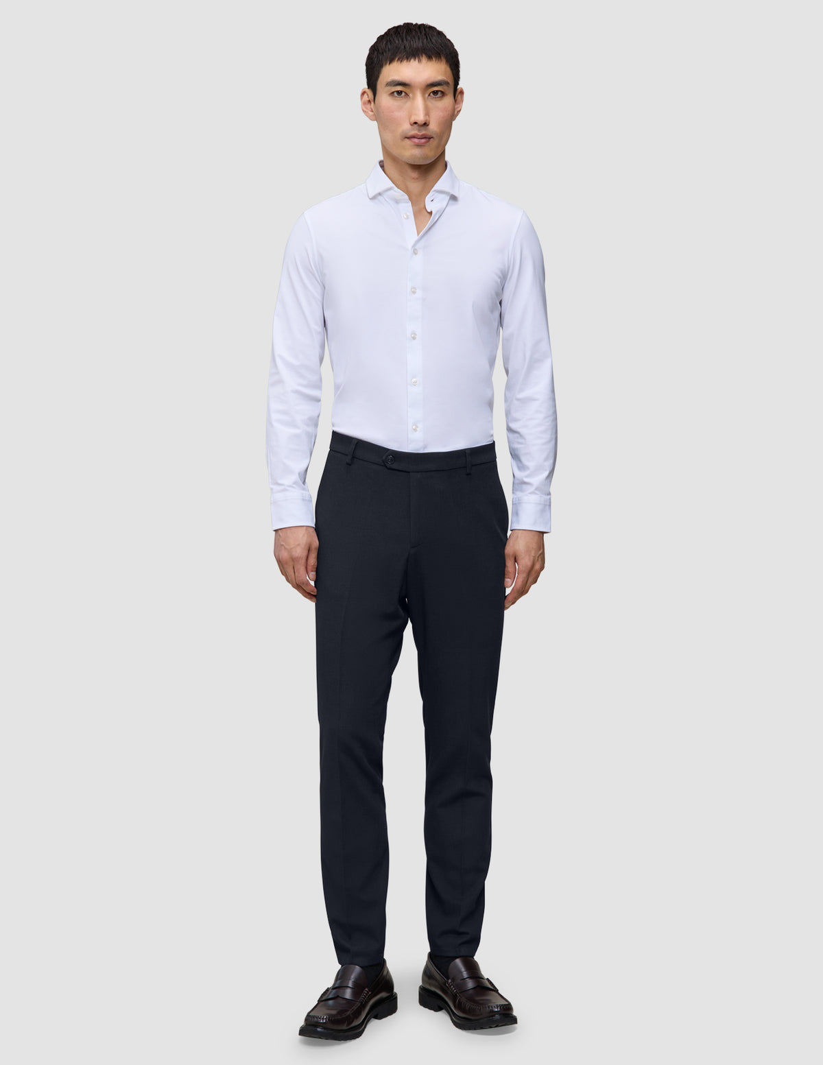 En man bär en vit skjorta med knappar, Motion Suit-byxor i smal passform i midnattblått och bruna loafers.