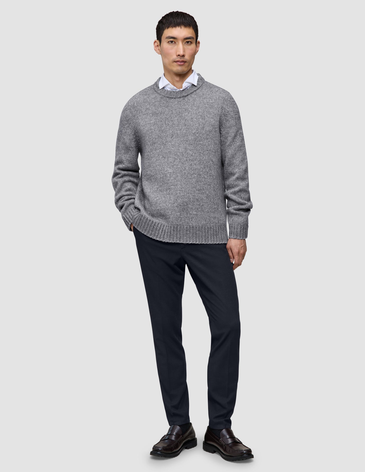 En man i en grå tröja, en vit skjorta med krage och midnattsblå Motion Suit Pants Slim samt loafers.