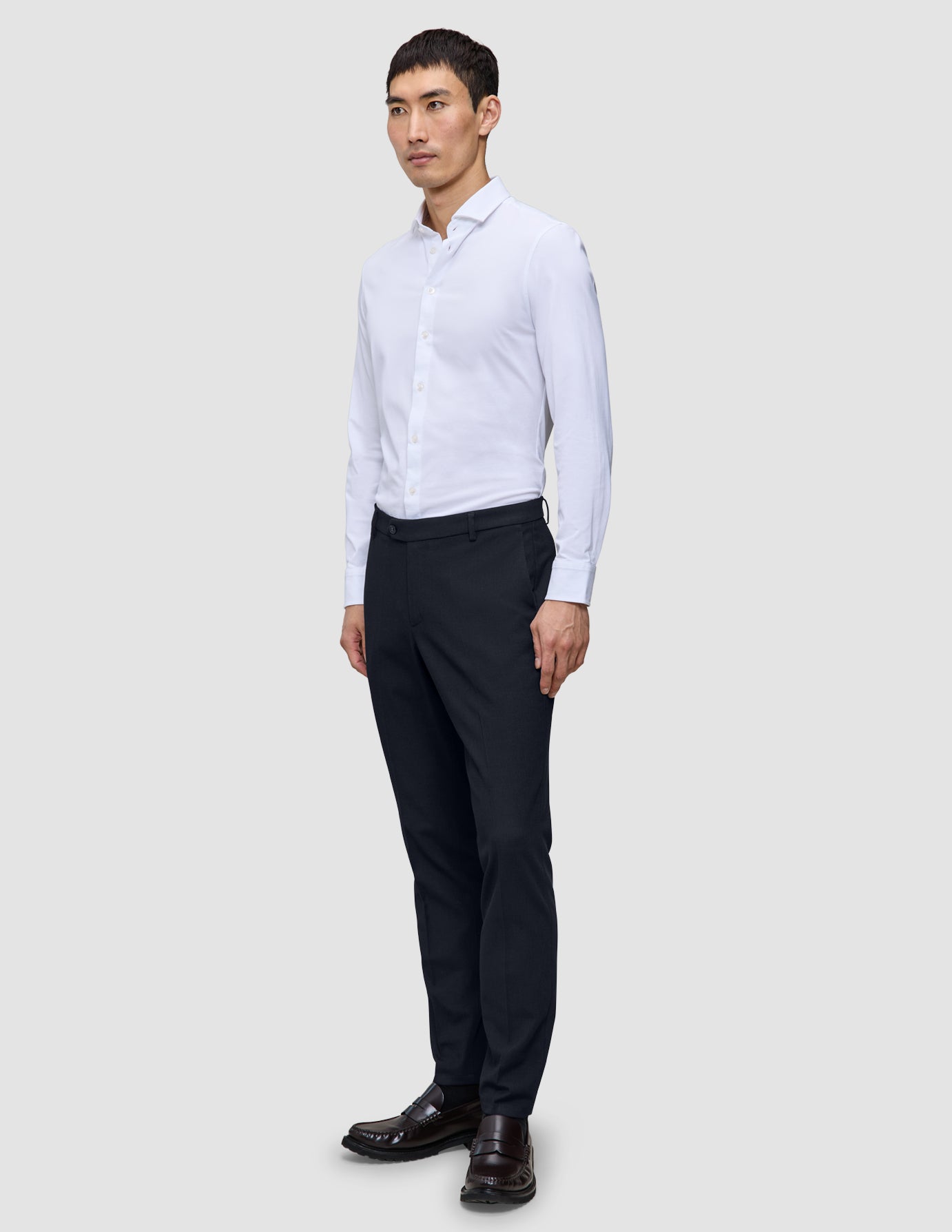 En man klädd i en vit skjorta, ett par slim fit-byxor av modellen Motion Suit Pants Slim i midnattsblått och mörka läderskor.