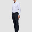 En man klädd i en vit skjorta, ett par slim fit-byxor av modellen Motion Suit Pants Slim i midnattsblått och mörka läderskor.