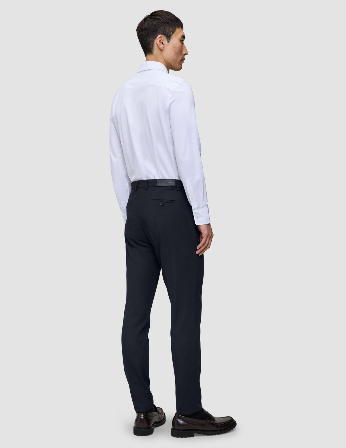 En person sedd bakifrån, klädd i en vit skjorta, Motion Suit-byxor i modell Slim i färgen Midnight Blue och mörka loafers.