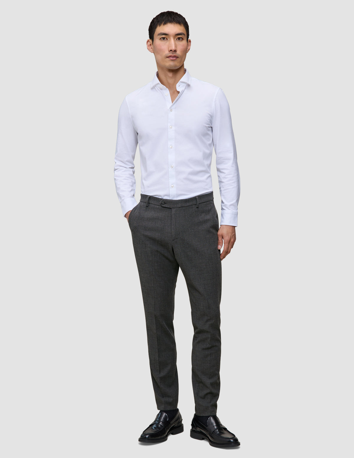 En man klädd i en vit skjorta, byxor av modellen Motion Suit Pants Slim Pepper Grey och svarta loafers, som speglar skandinavisk design.