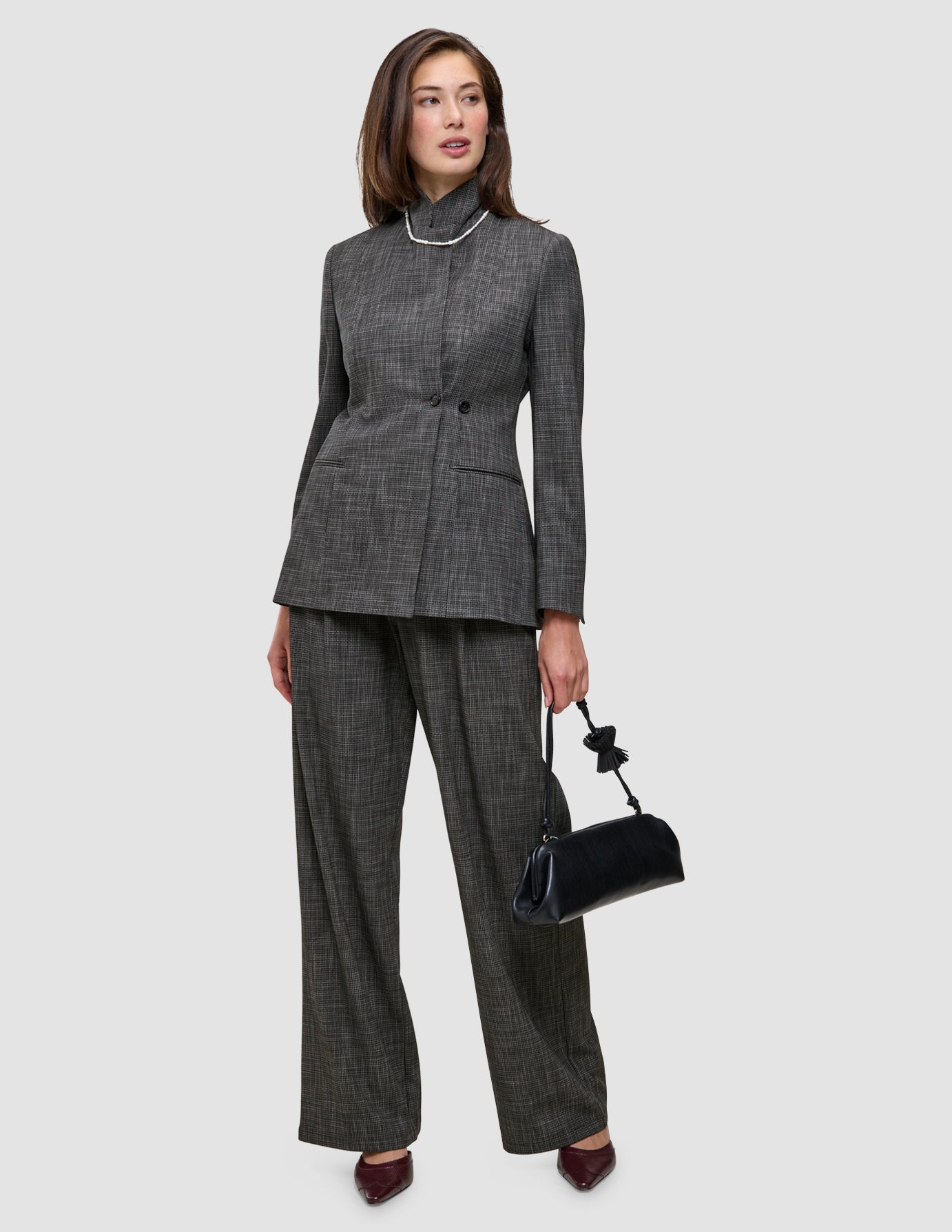 En kvinna bär kostymen The Suit with a Statement i kolgrått, bestående av en mönstrad kavaj, byxor med vida ben och en handväska.