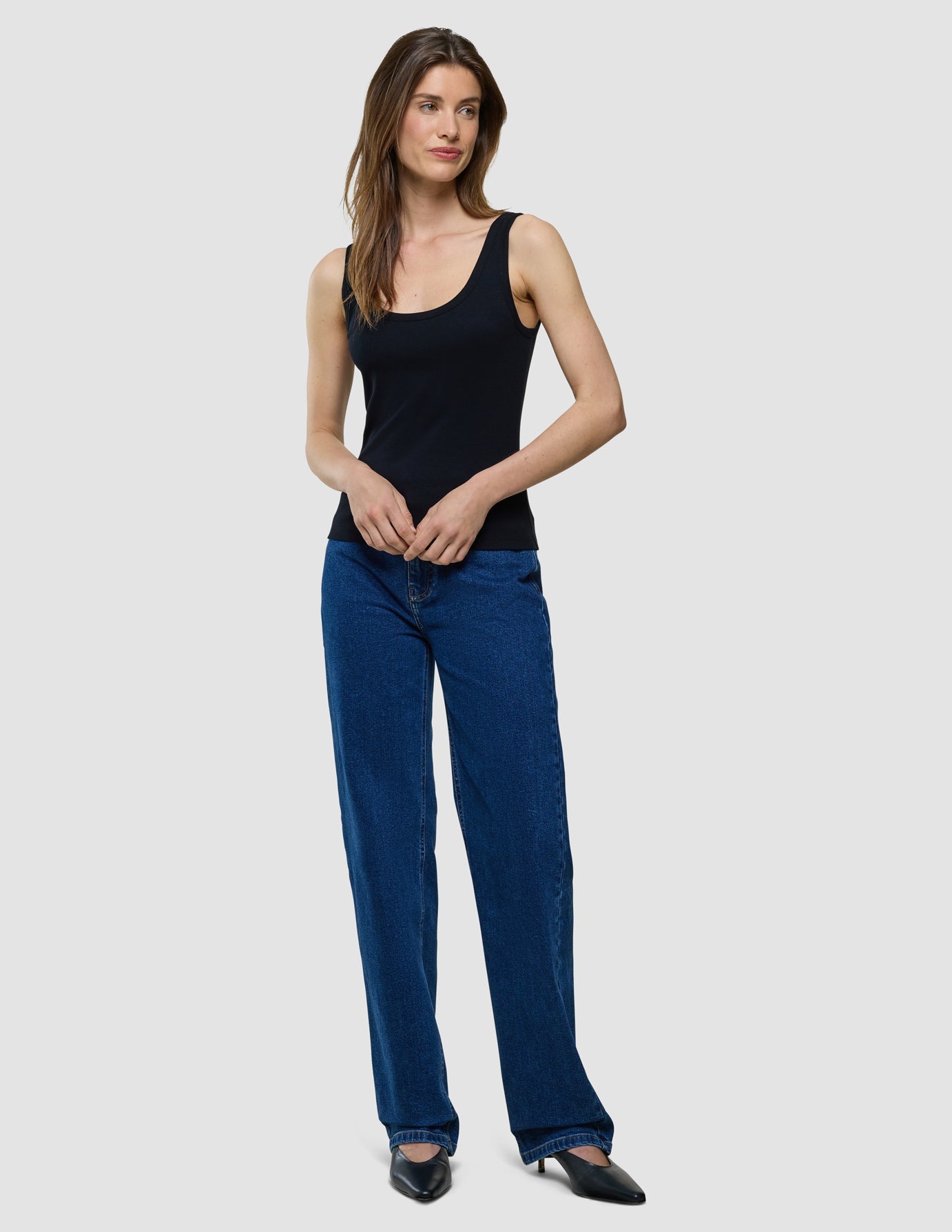 En kvinna klädd i en svart ribbad linne och blå jeans.