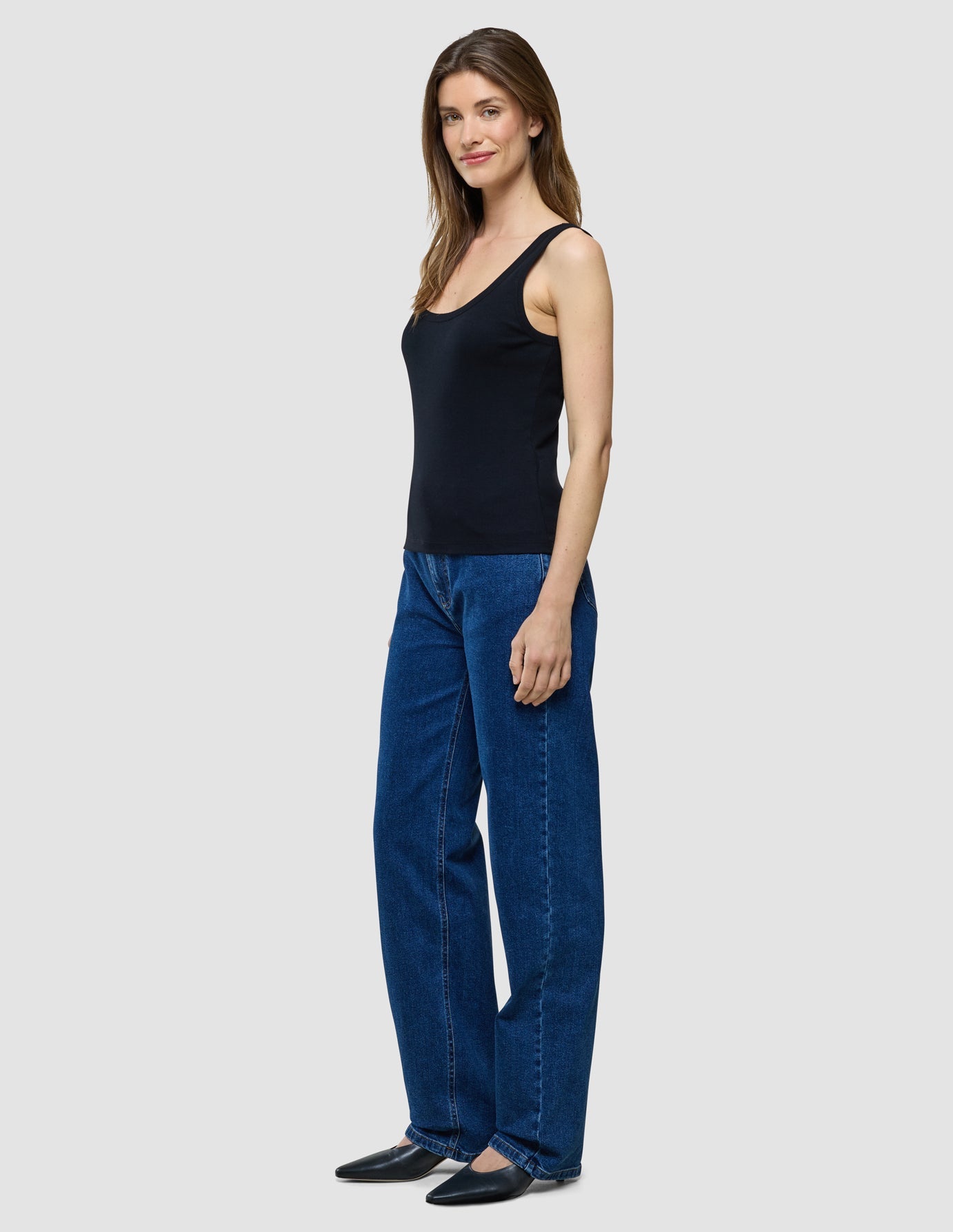 En kvinna som står där klädd i en svart ribbad linne och blå jeans.