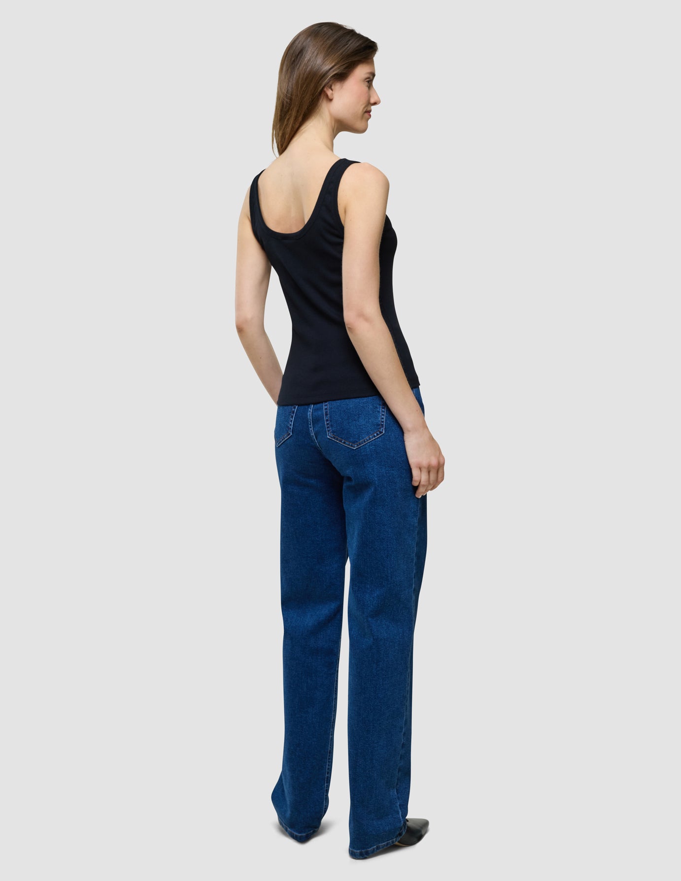 En kvinna sedd bakifrån, klädd i en svart ribbad linne och blå jeans.