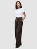 En kvinna i en vit t-shirt bär mörkbruna byxor med vida ben, modellen Serene Pants Wide Walnut Herringbone, med handen i fickan.