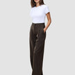 En kvinna i en vit t-shirt bär mörkbruna byxor med vida ben, modellen Serene Pants Wide Walnut Herringbone, med handen i fickan.
