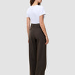 Kvinna i en vit t-shirt och mörkbruna, högmidjade, randiga byxor med vida ben av modellen Serene Pants Wide Walnut Herringbone.