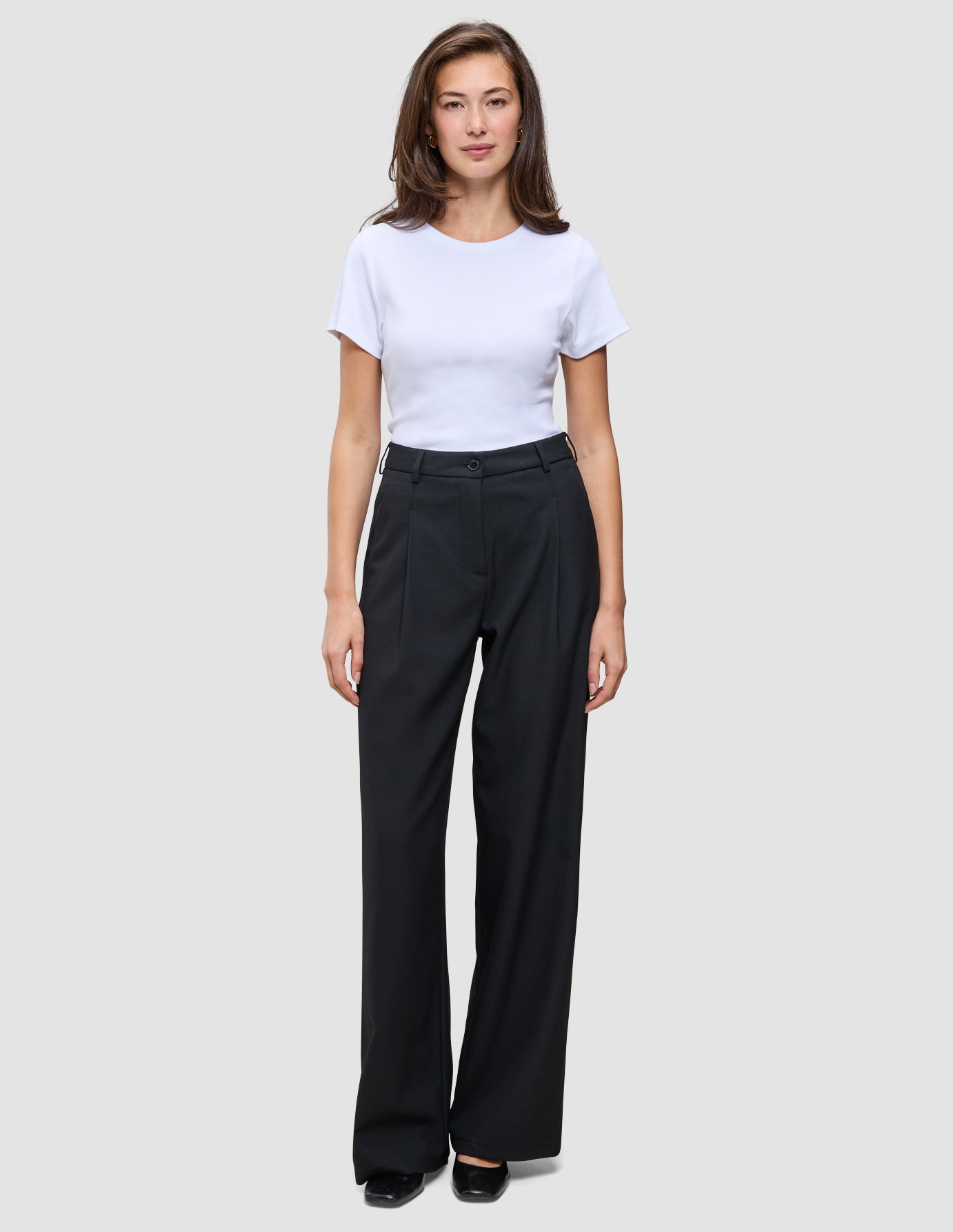 En kvinna klädd i en vit t-shirt och svarta, vidbyxor av modellen Serene Pants Wide Black.