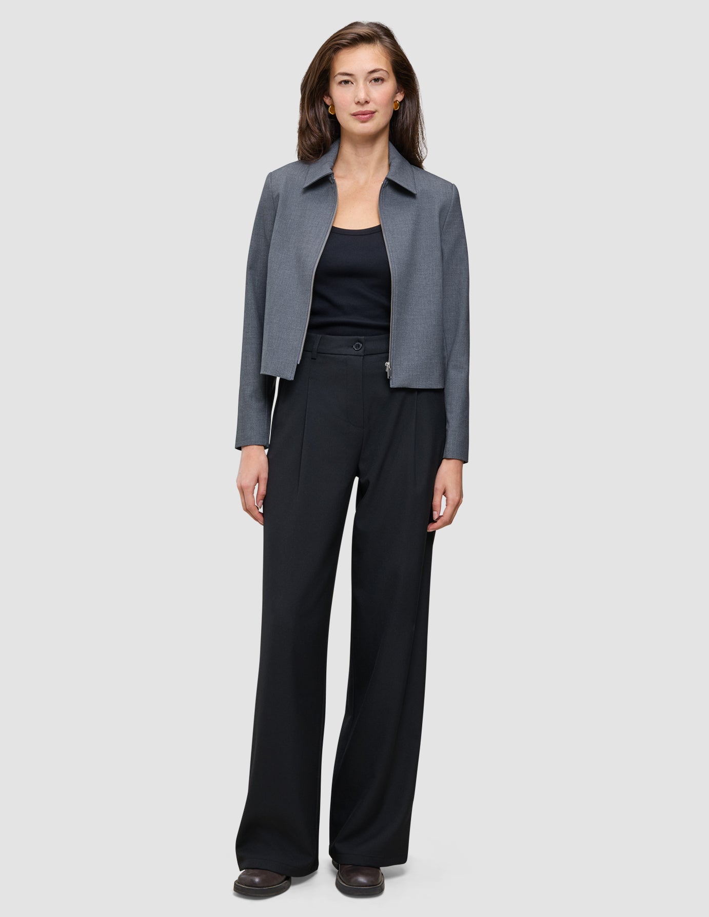 En person i en grå jacka med krage och en svart överdel bär ett par högmidjade Serene Pants Wide Black.