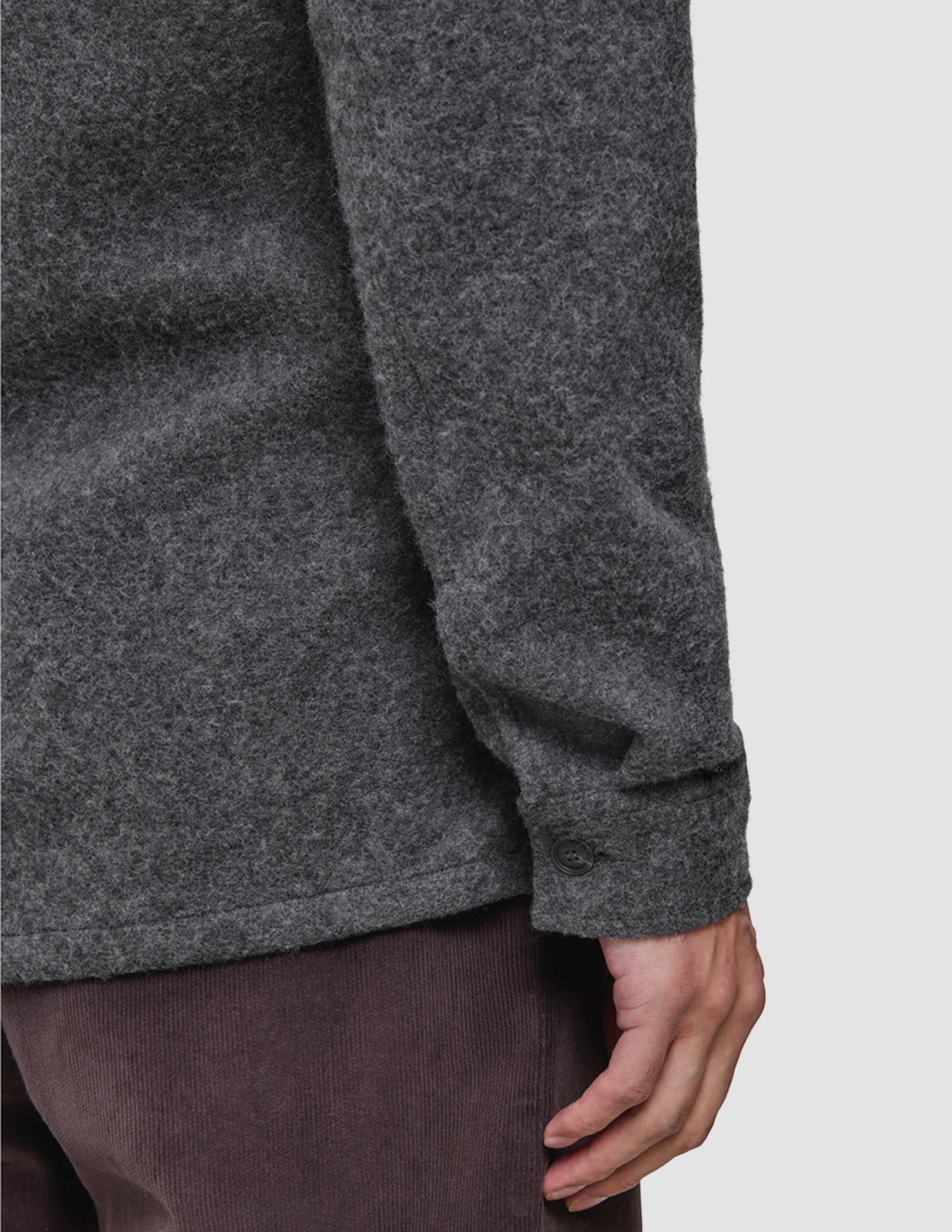 Närbild på en person klädd i en avslappnad och genomtänkt överskjorta i kolgrå ull och mörkbruna Marco Jeans.