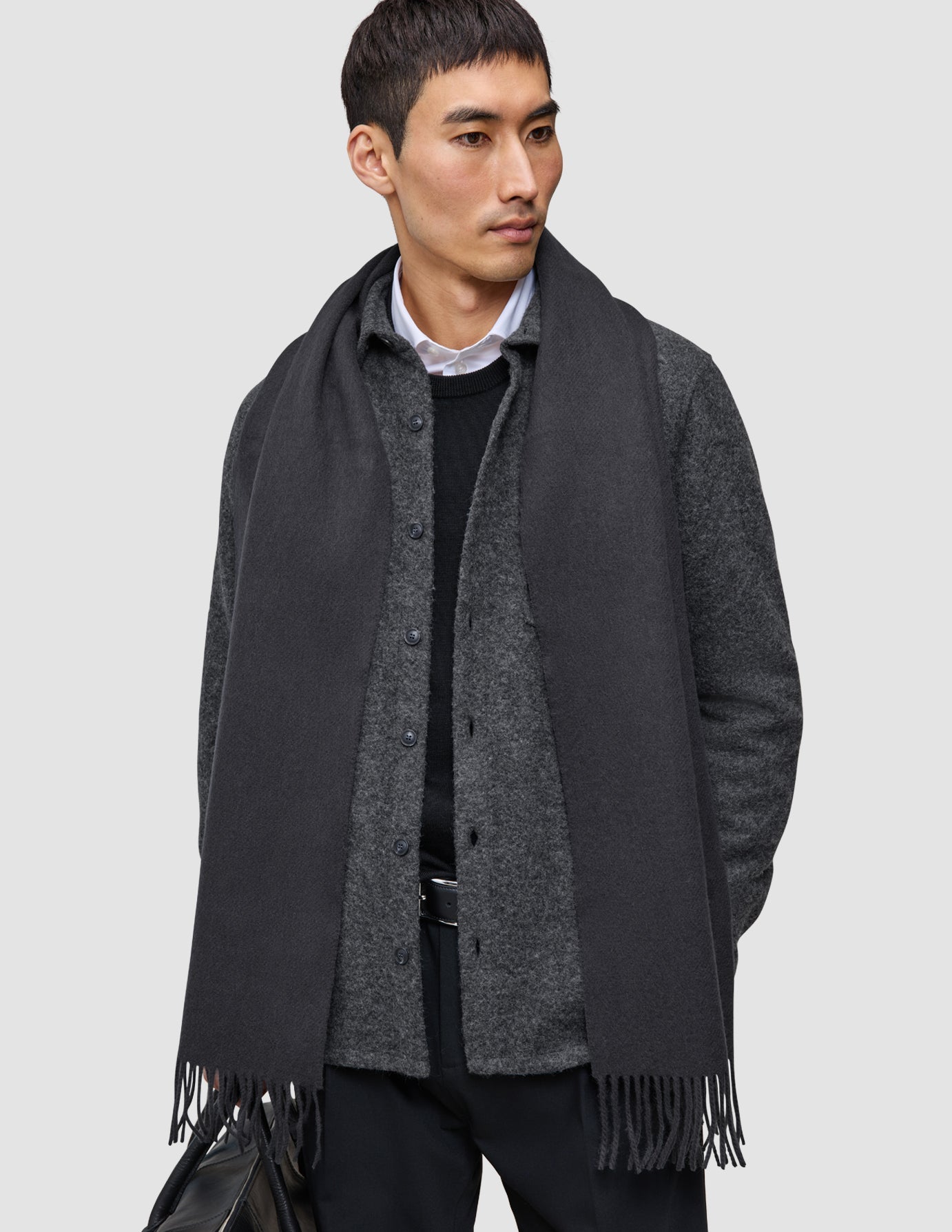 En man bär ett välfungerande lager-på-lager-outfit, bestående av en mörkgrå halsduk över en grå skjorta med knappar och en högkvalitativ merinoullströja.