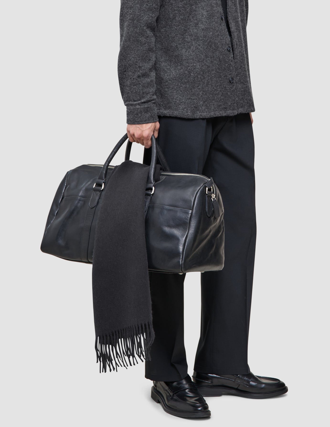 En person bär en merinoullströja från Layers that work och håller i en svart läderresväska med en mörk halsduk draperad över handtaget.