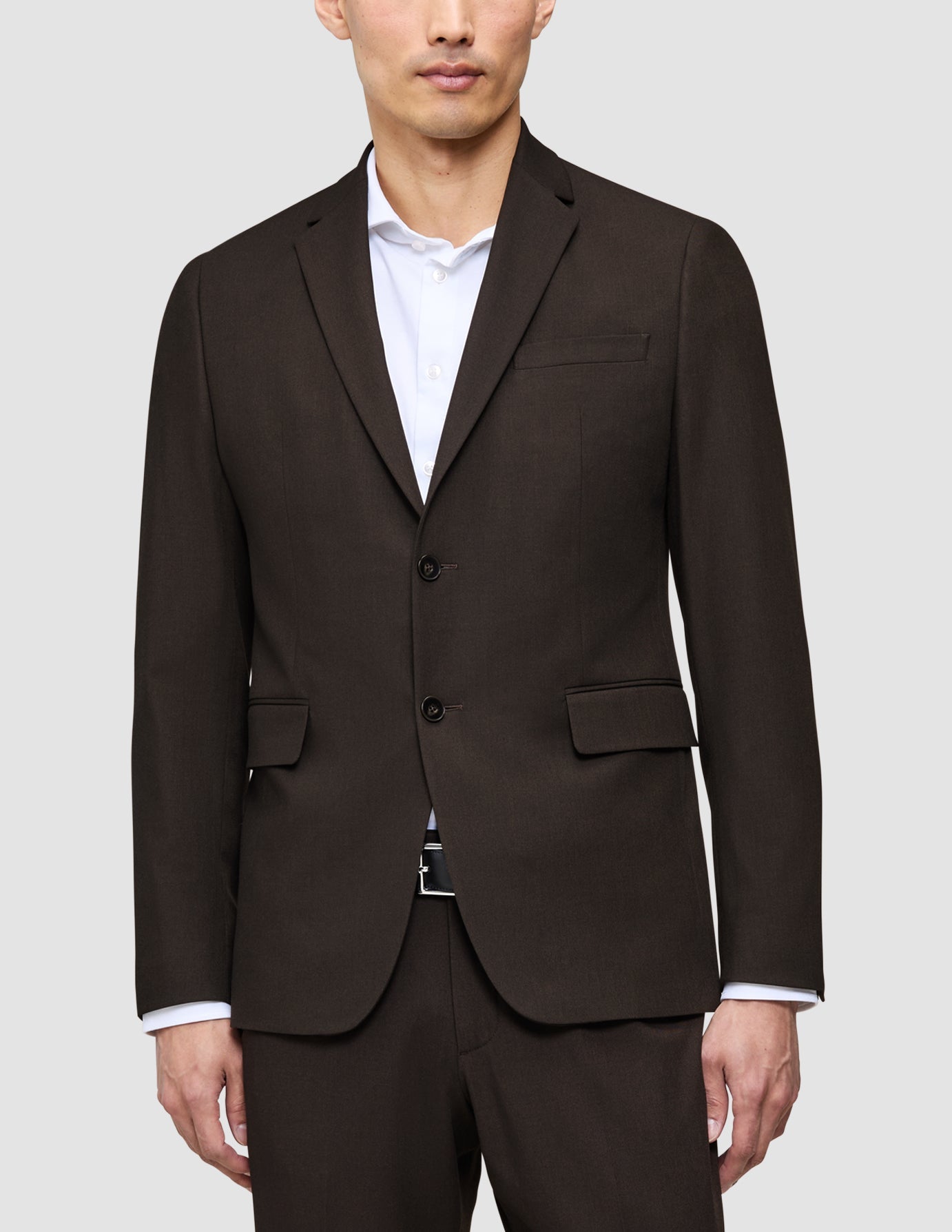 En man klädd i en mörkbrun The suit that does it all-jacka över en vit skjorta av hög kvalitet.
