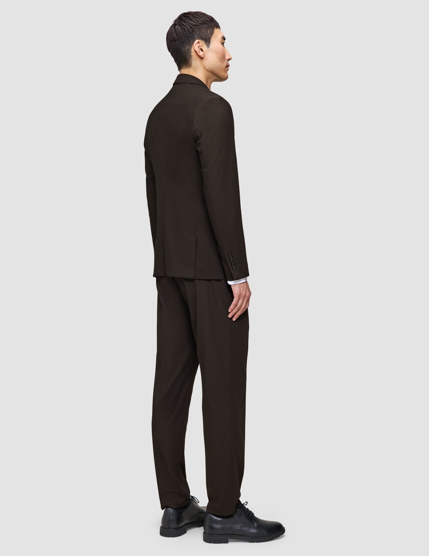 En man i profil bär The suit that does it all i mörkbrunt tillsammans med svarta kostymskor.