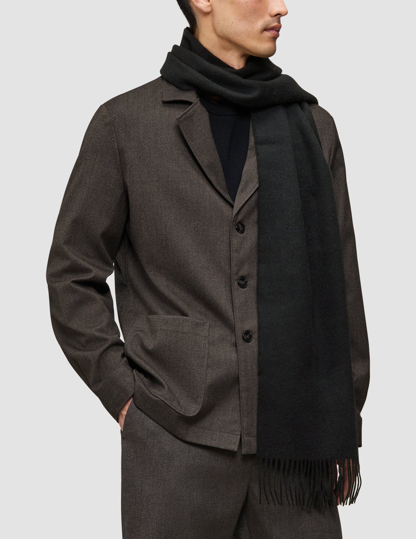 En person som bär en brun kostym av ett annat slag över en svart Premium Merino Knit-tröja och en halsduk.