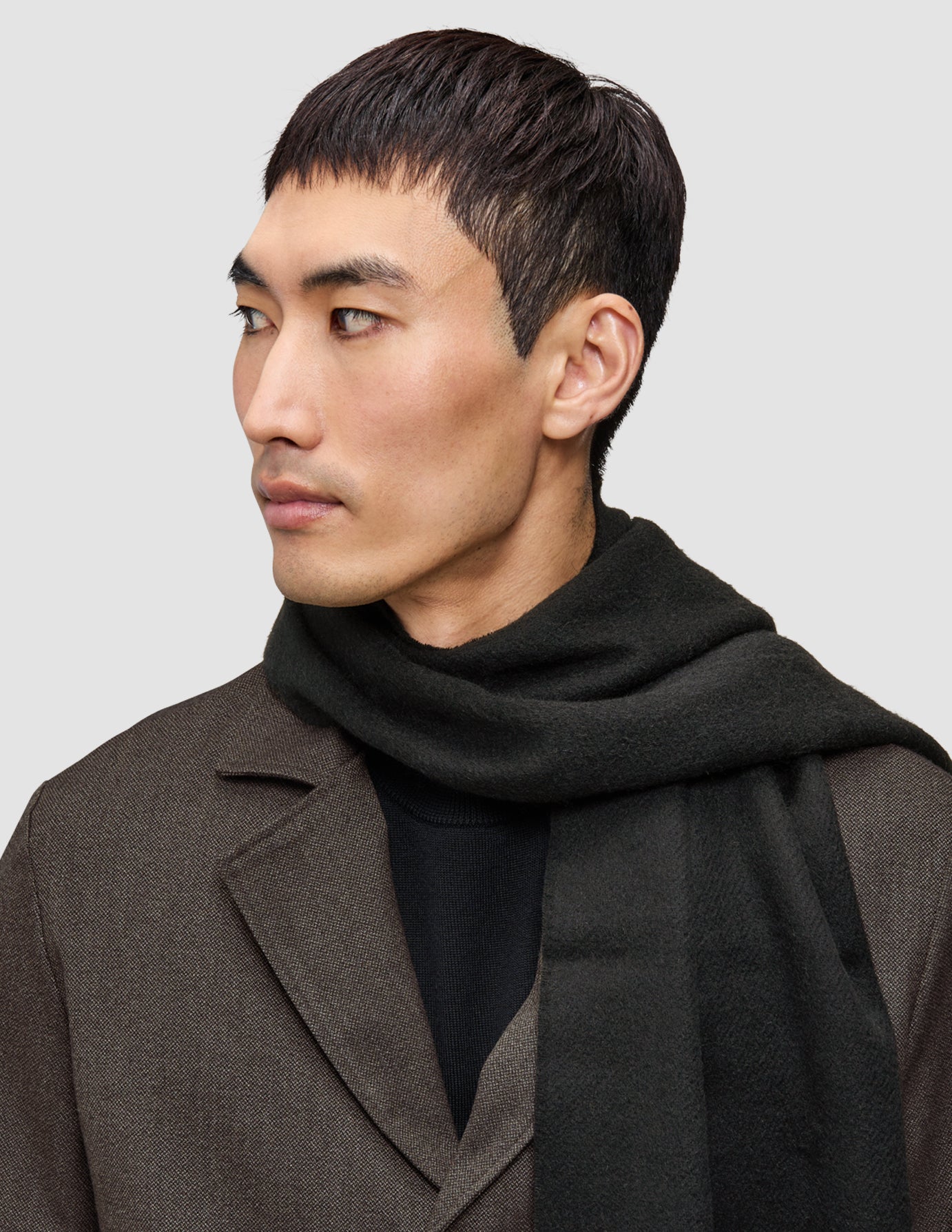 En man klädd i en annorlunda kostym, en overshirt från Atelier, en mörkgrön halsduk och en stickad tröja i Premium Merino.