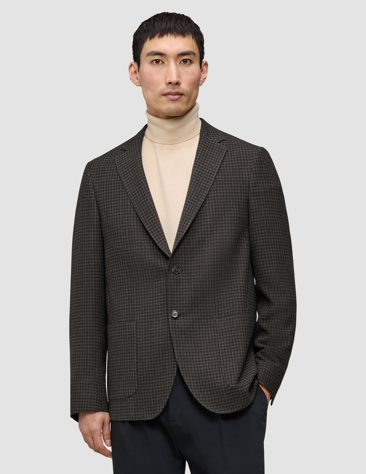 En man klädd i en mörkbrun rutig Timeless-ullblazer i smal passform över en beige polotröja, vilket återspeglar klassisk skandinavisk design.