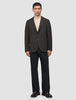 En man bär en mörkbrun rutig Timeless Wool Blazer Slim över en krämfärgad polotröja och mörka byxor.