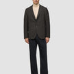 En man bär en mörkbrun rutig Timeless Wool Blazer Slim över en krämfärgad polotröja och mörka byxor.