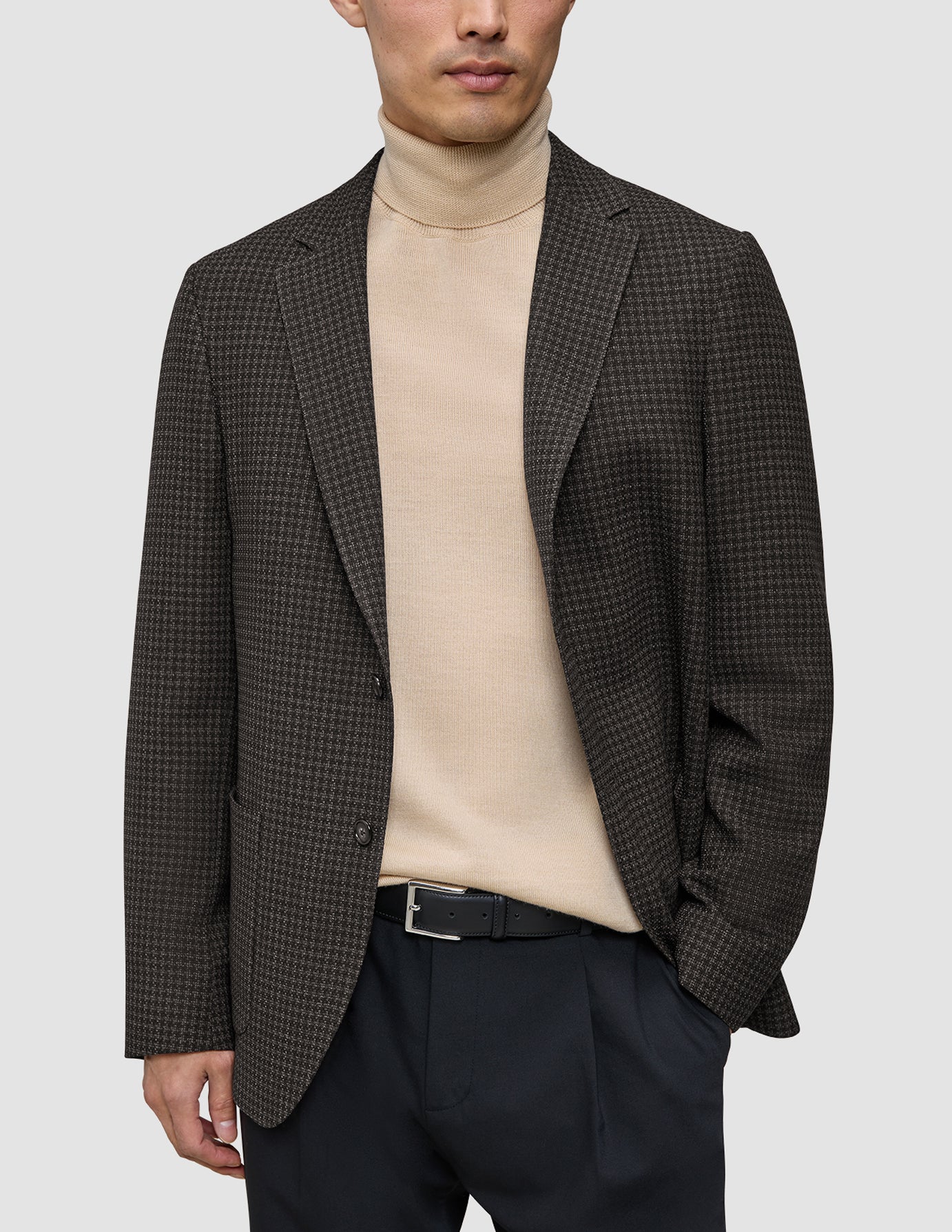 En person som bär en mörkbrun rutig Timeless Wool Blazer Slim över en beige polotröja och svarta byxor.