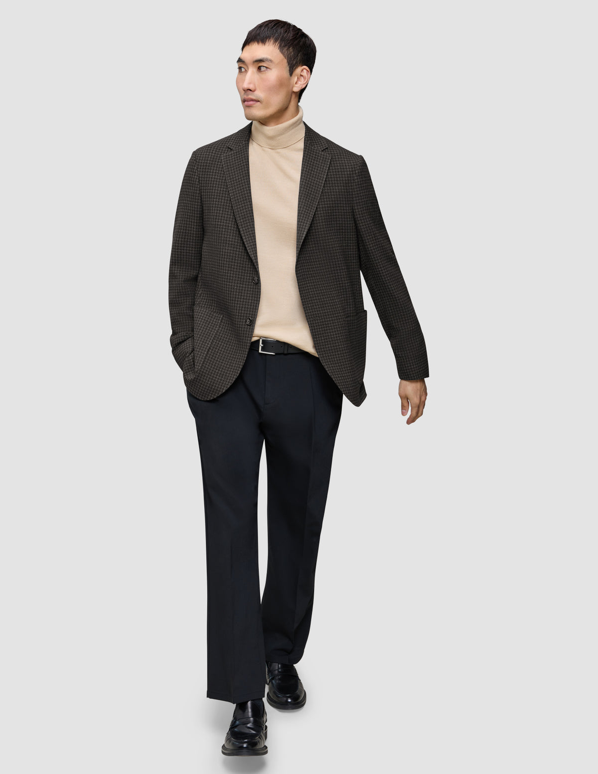 En man klädd i en mörkbrun rutig Timeless-ullblazer i smal passform, en beige polotröja, svarta byxor och loafers.