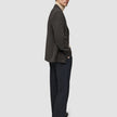En person klädd i en mörkbrun rutig Timeless Wool Blazer Slim, en beige polotröja och mörka byxor.
