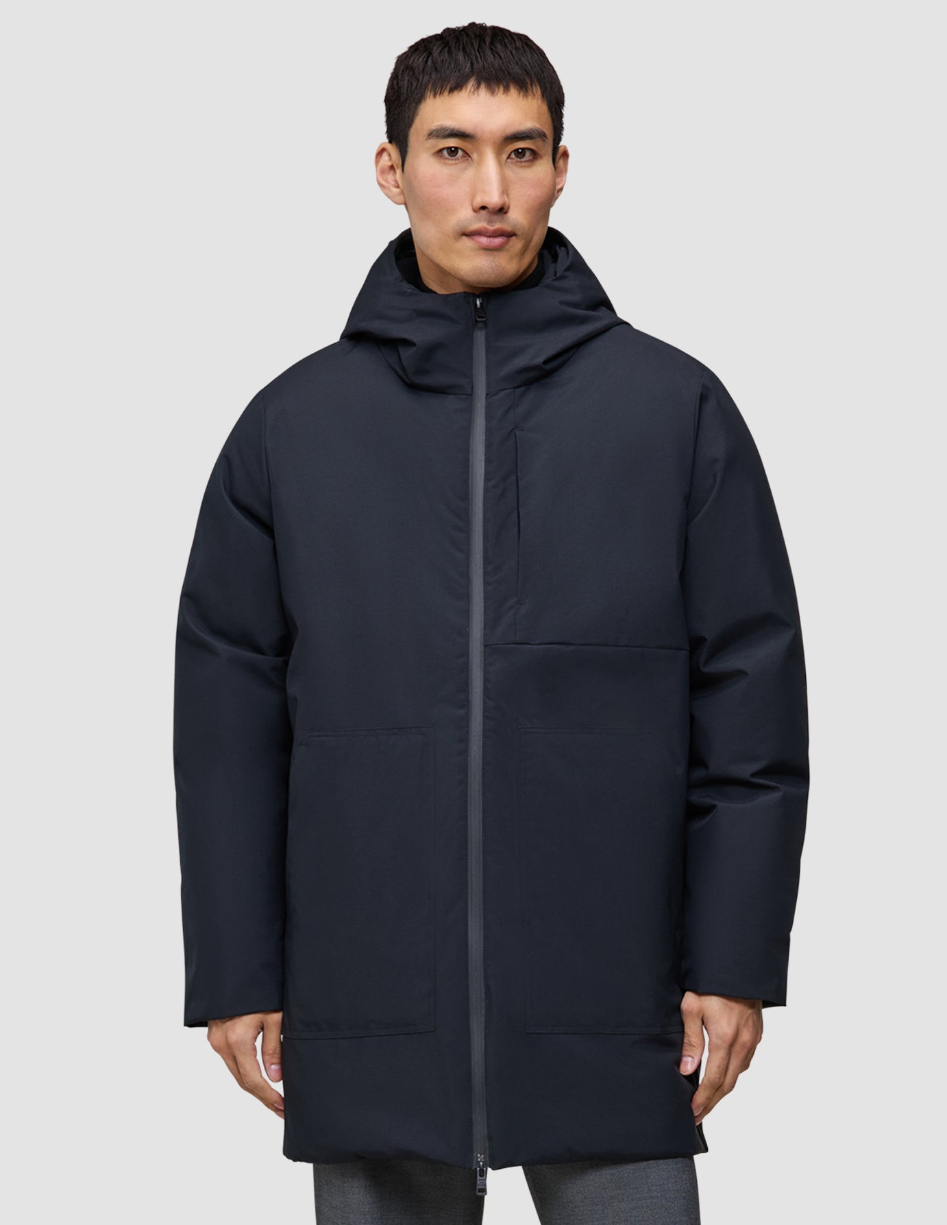 En man klädd i en svart, knälång Utility Jacket Black med huva.