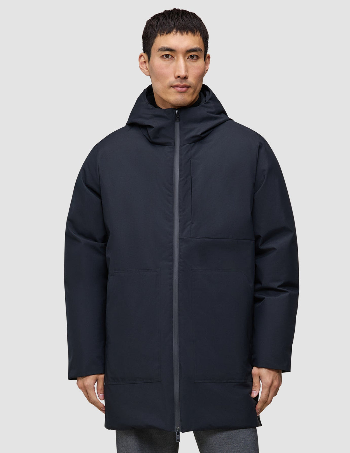 En man klädd i en svart, knälång Utility Jacket Black med huva.