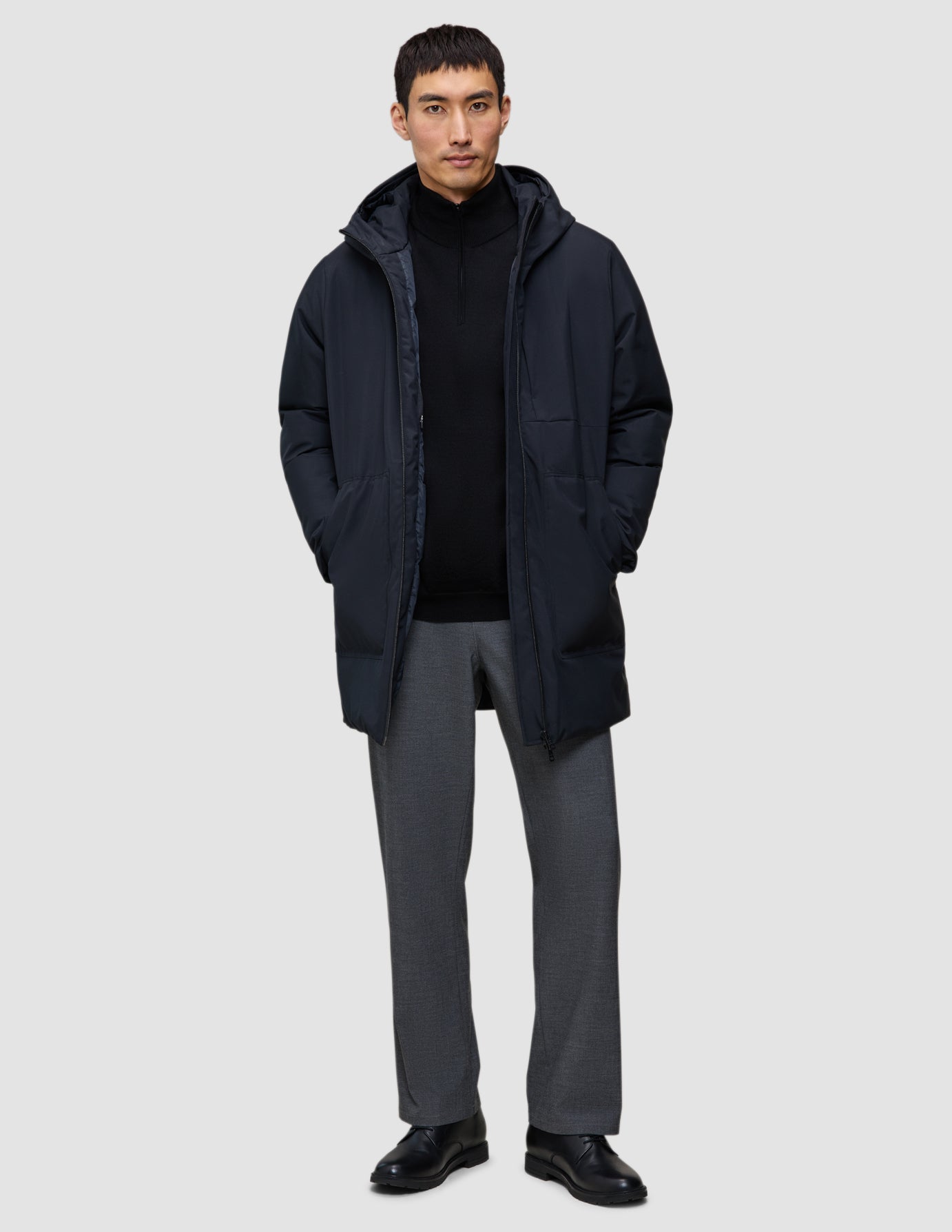 En man bär en svart Utility Jacket över en svart tröja med kvartslås och grå byxor.