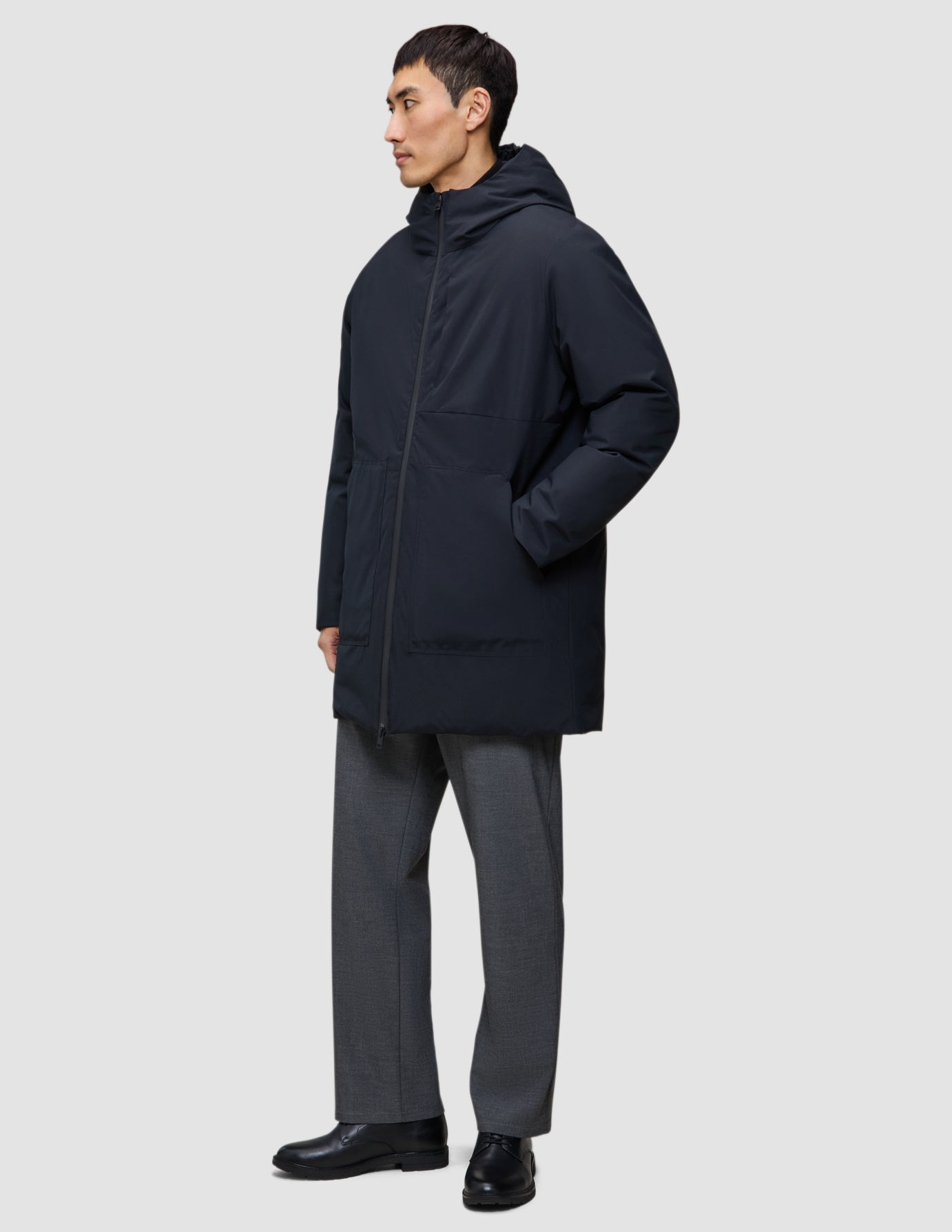 En person klädd i en vind- och vattentät svart Utility Jacket Black med dragkedja framtill och grå byxor.