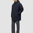 En person klädd i en vind- och vattentät svart Utility Jacket Black med dragkedja framtill och grå byxor.