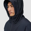 En person som bär en svart Utility Jacket Black med huvan uppe, en jacka som är vind- och vattentät.