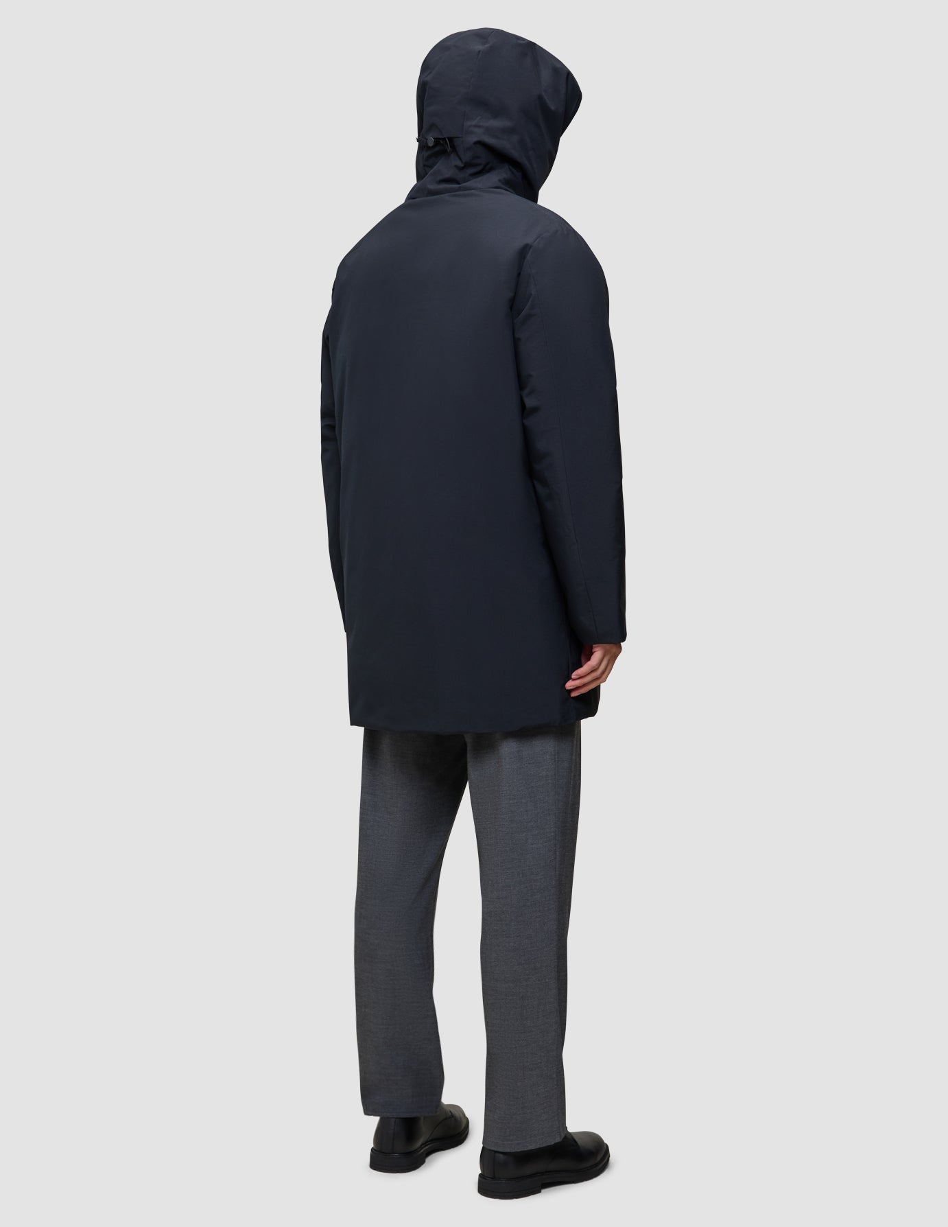 En person sedd bakifrån, klädd i en svart Utility Jacket och svarta och grå byxor.