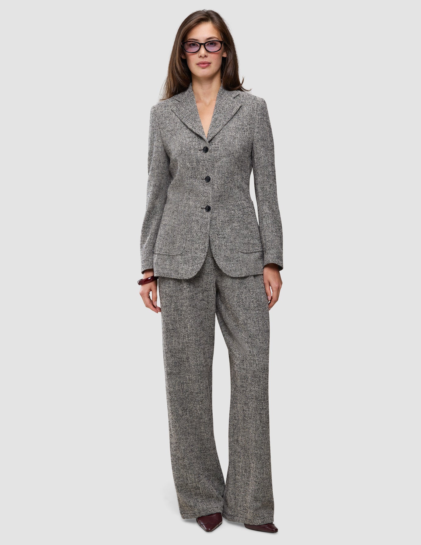 En kvinna klädd i en grå byxdräkt i fiskbensmönster från Women Ashryn Pants Wide Domino Herringbone, med en knäppt kavaj.