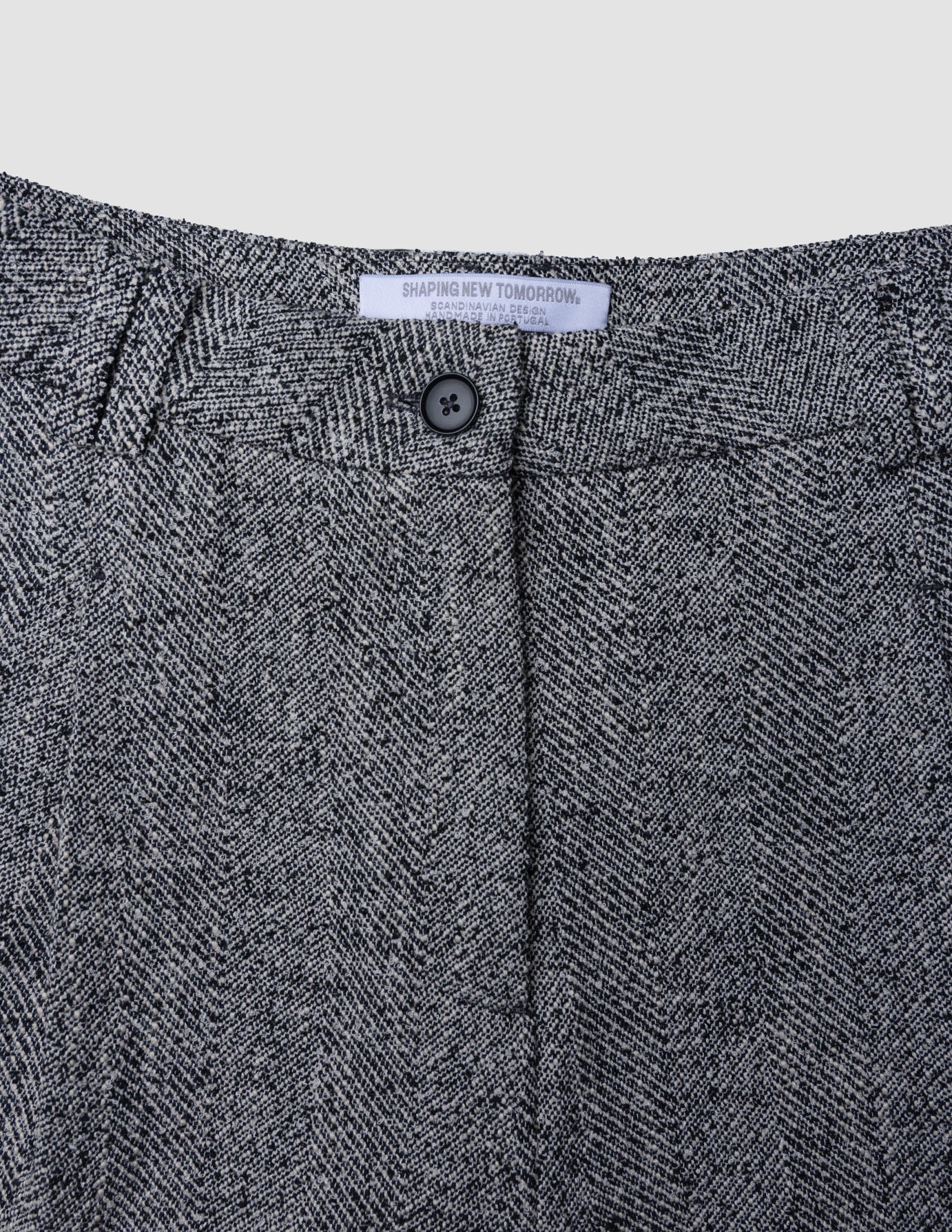Närbild på Ashryn-byxor för damer, modell Wide Domino Herringbone, med hög midja och ett grått och svart fiskbensmönster.