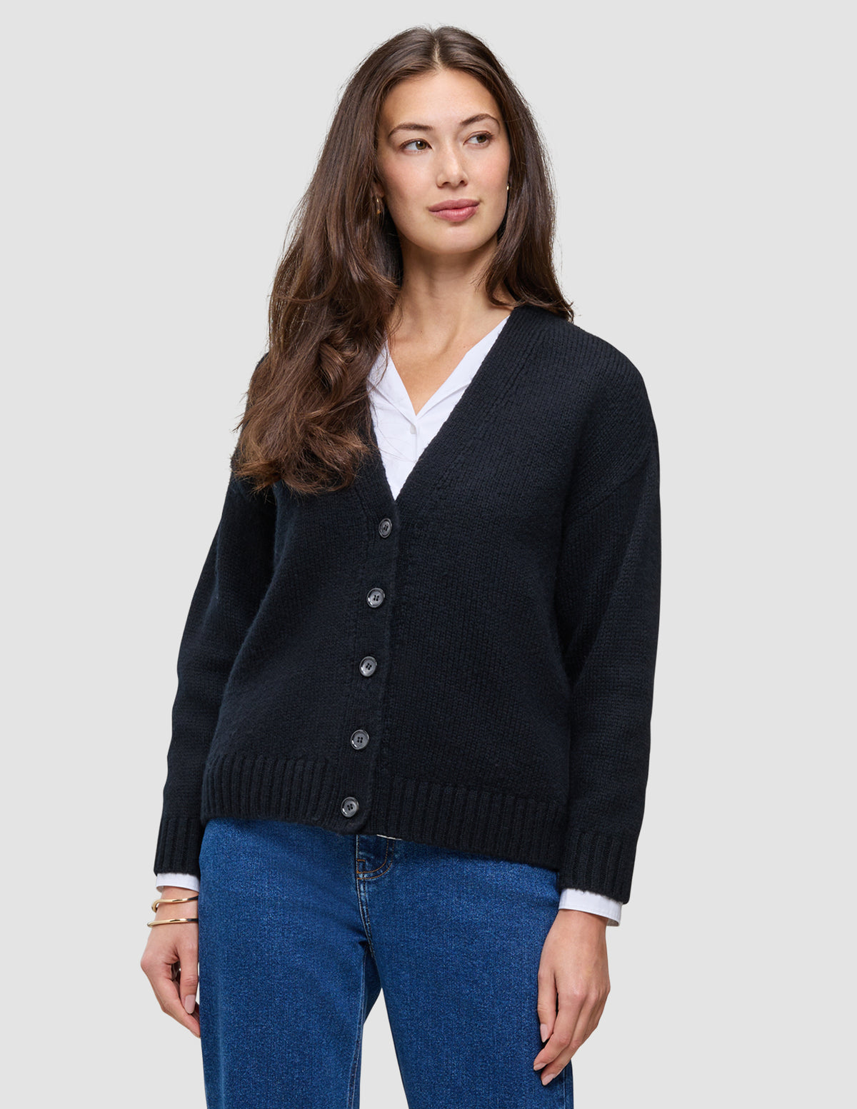 En kvinna som bär en svart, tjock och mjuk stickad kofta i ull från kollektionen Women över en vit skjorta med krage och blå jeans.